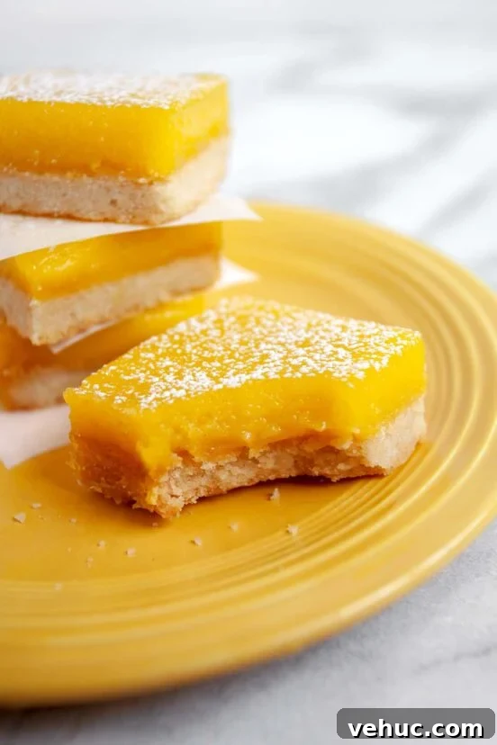 Classic Italian Rainbow Cookies Recipe You’ll Love 7 Yellow plate with four lemon bars sprinkled with powdered sugar, one with a bite take out of it.