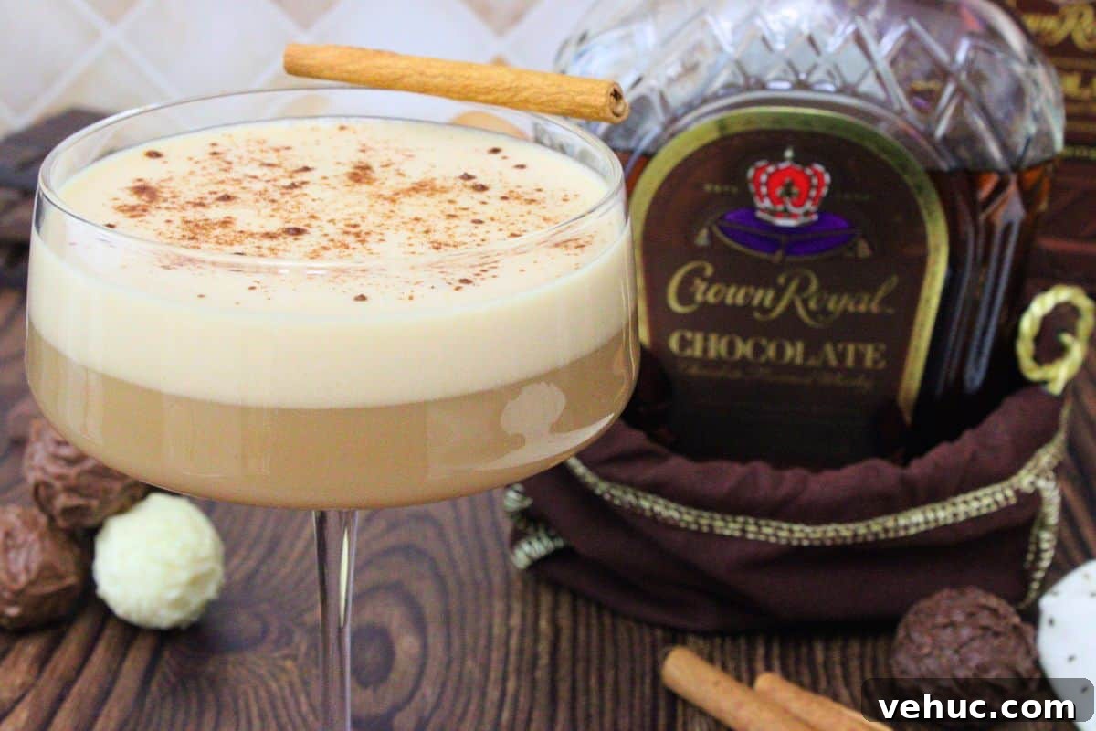 12 Irresistible Chocolate Crown Royal Cocktails to Try Tonight 7 closeup view of chocolate whiskey flip dusted with cinnamon and a cinnamon stick next to chocolate crown royal bottle