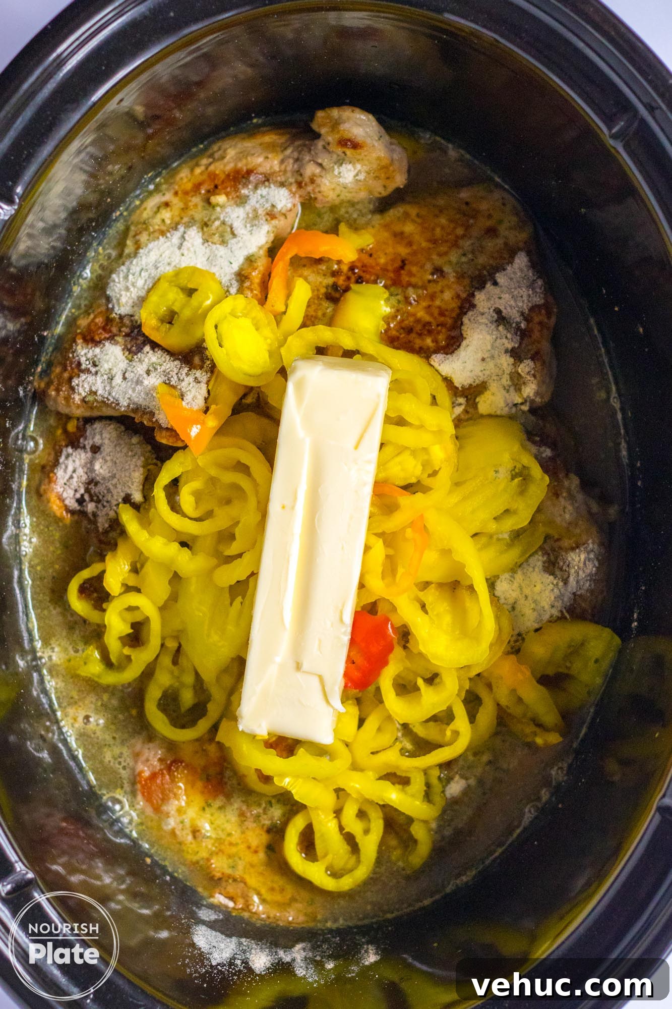 Mississippi-Style Slow Cooker Pork Chops You’ll Love 5 Boneless pork chops in a black slow cooker, with peppers and a stick of butter before cooking