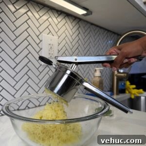 Creamy Garlic Mashed Potatoes Recipe 8 Potatoes being mashed in a bowl with a potato ricer.