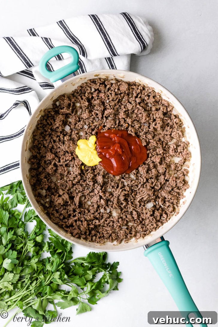 Ketchup and mustard over ground beef in a pan.