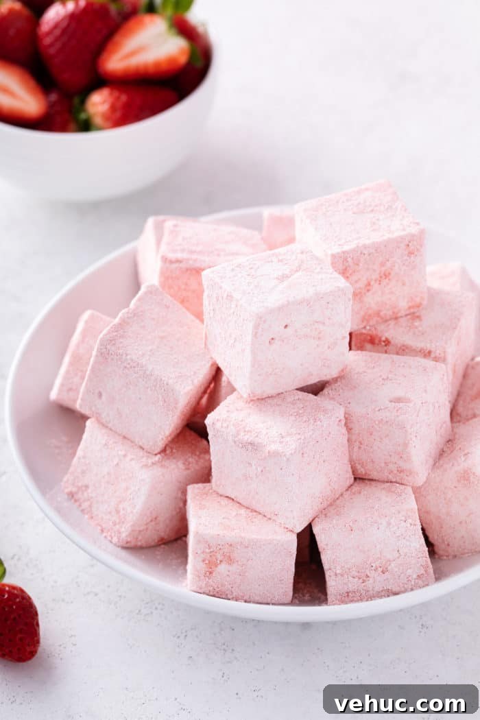 Homemade Strawberry Marshmallows: Soft, Fluffy Recipe 4 White bowl filled with strawberry marshmallows. A bowl of sliced strawberries is in the background.