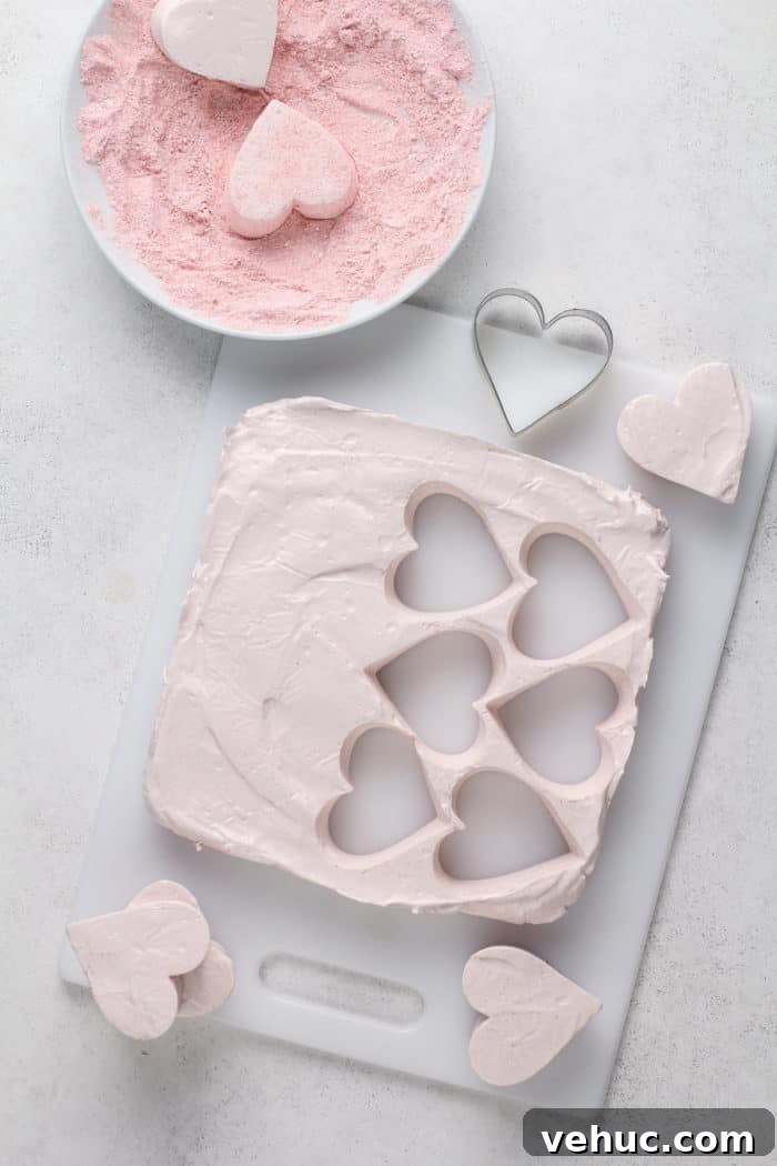 Homemade Strawberry Marshmallows: Soft, Fluffy Recipe 9 Cutting heart shapes out of a slab of strawberry marshmallows on a white cutting board.