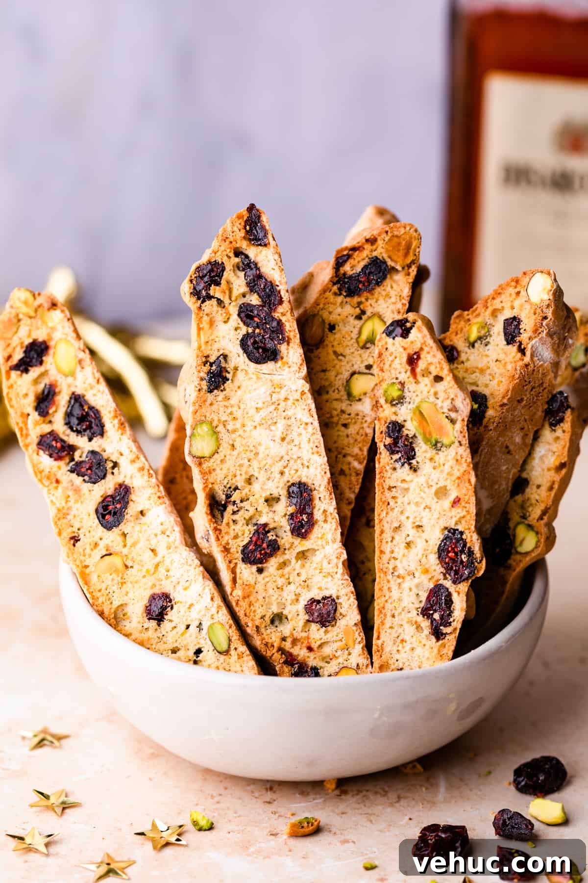 Cranberry Almond Biscotti Recipe for Crunchy Coffee Cookies 12 biscotti cookies standing up inside of ceramic bowl with some dried cranberries on side.