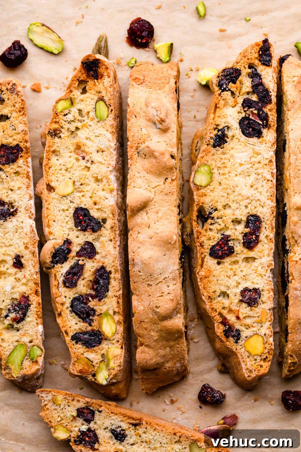 Cranberry Almond Biscotti Recipe for Crunchy Coffee Cookies 10 crispy cranberry biscotti slices with crushed pistachios and dried cranberries scattered around them.