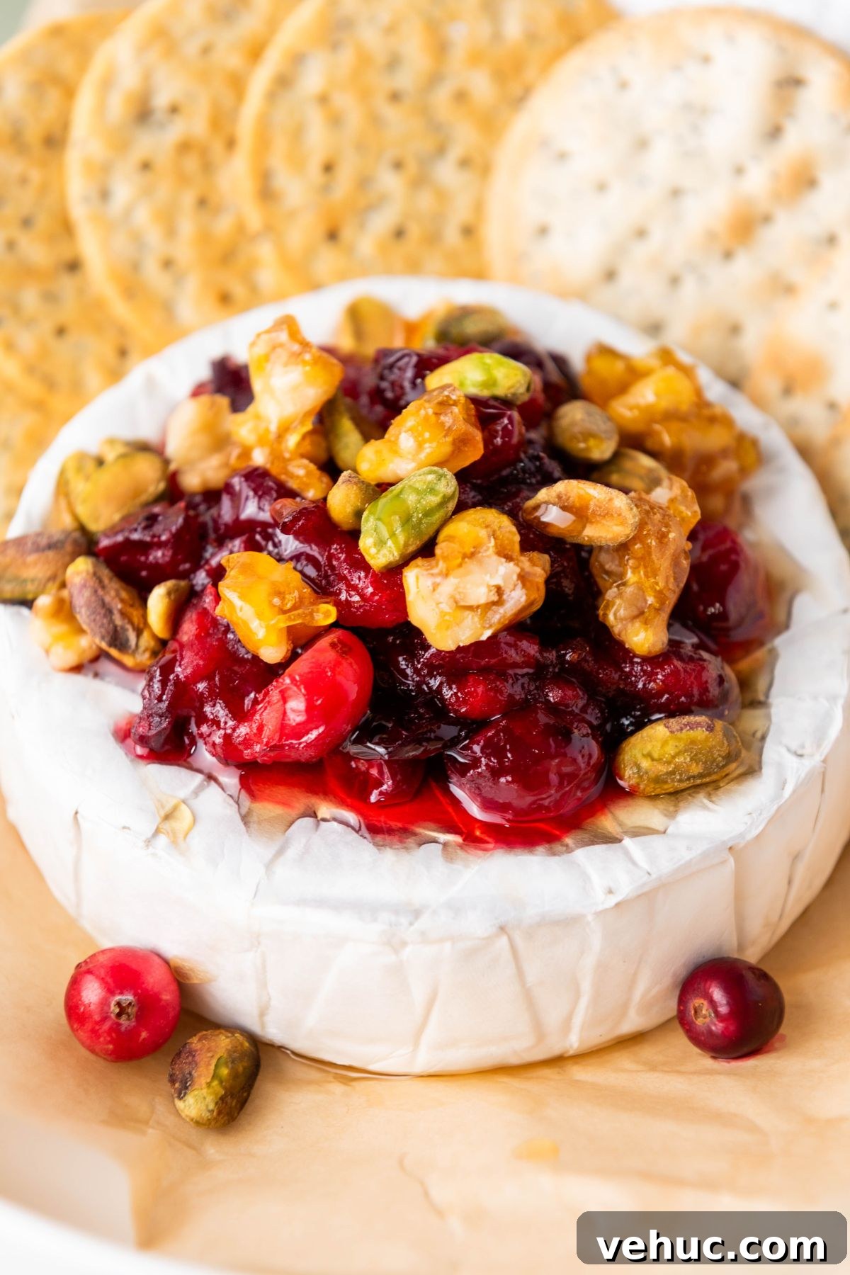 Baked Brie with Honey and Crispy Puff Pastry 2 A round block of brie cheese, topped with nuts and cranberries, surrounded by crackers.