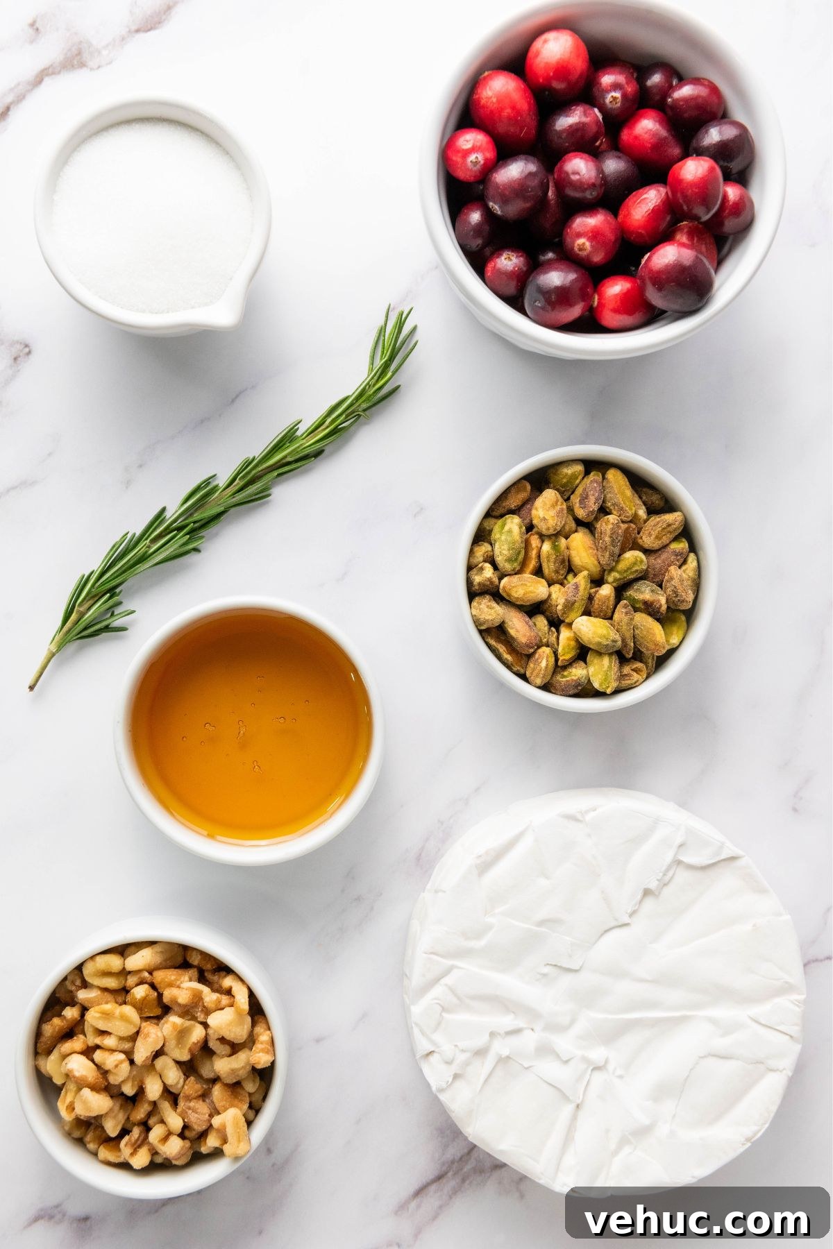 Baked Brie with Honey and Crispy Puff Pastry 3 Ingredients like brie cheese, cranberries, nuts, and honey, measured out in small bowls on a white marble table.