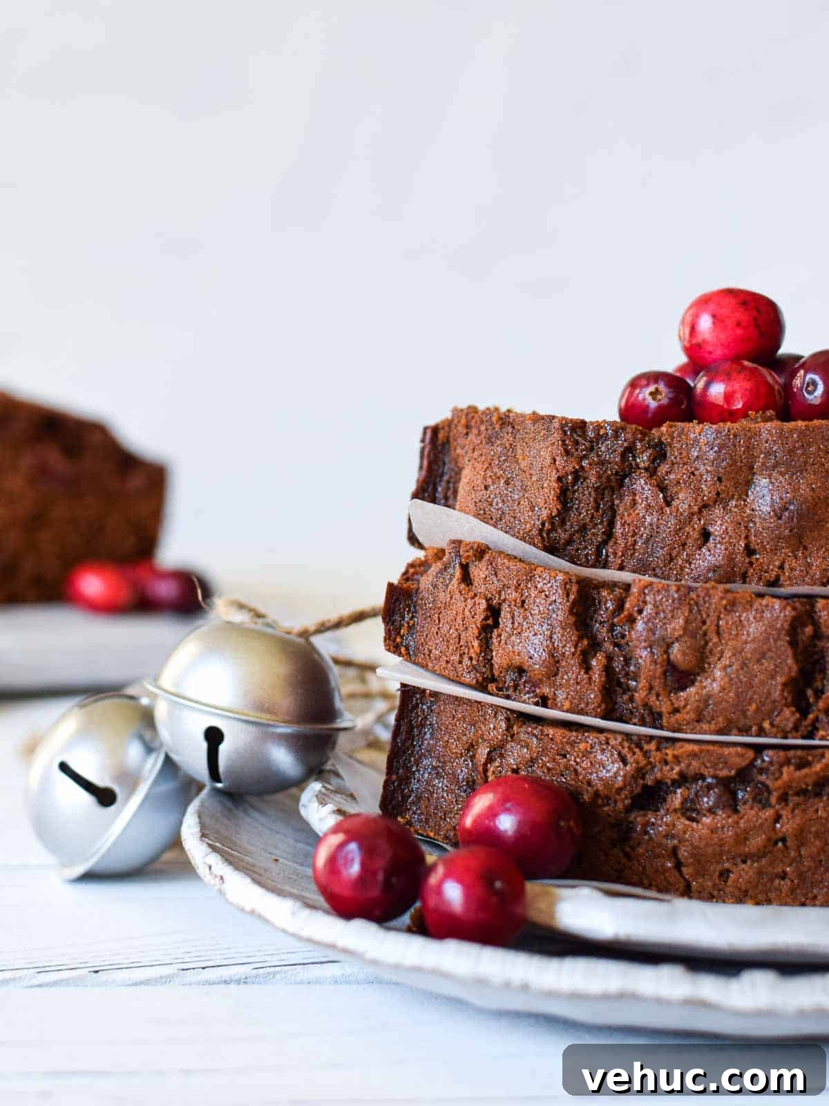 Cranberry Gingerbread Loaf Recipe with Zesty Ginger Glaze 3 Eye-level view of slices of cranberry loaf with cranberries and bells next to it.