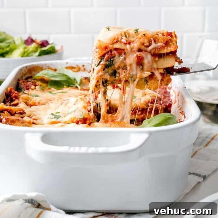 A slice of gluten-free lasagna lifted from a pan with cheese pull.