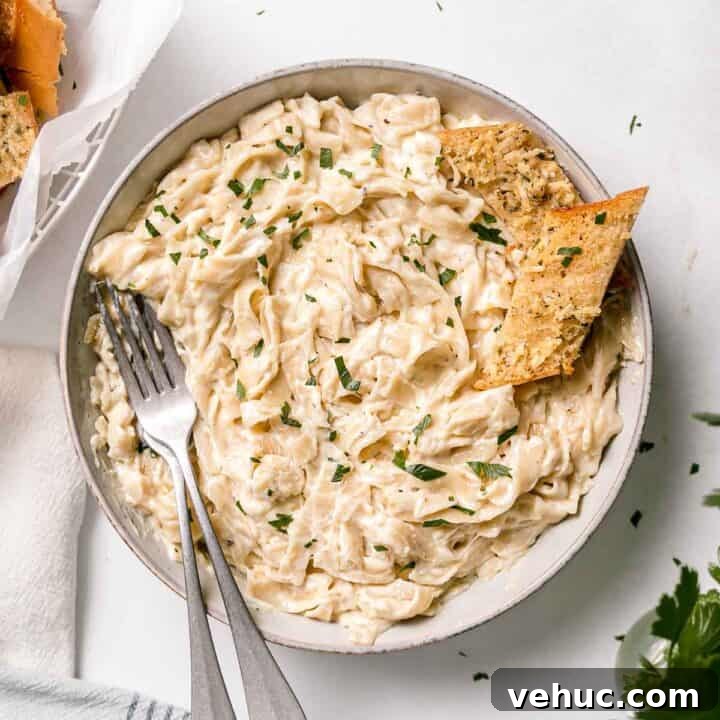 Gluten-free Fettuccini pasta in a large bowl with two forks and garlic bread to the side.