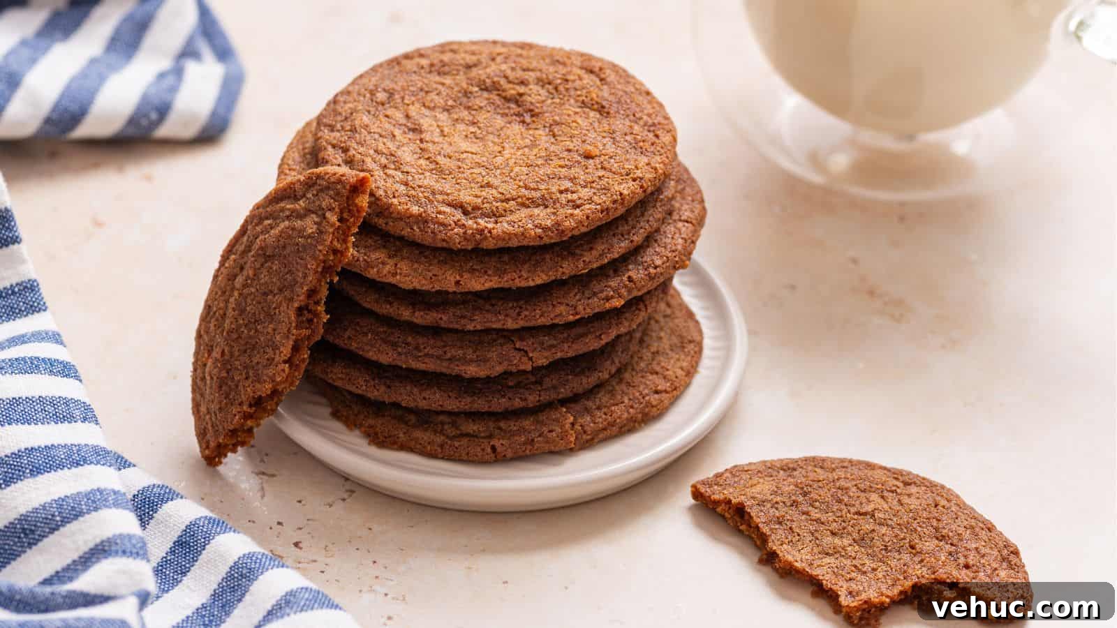 A stack of crisp brown cookies on a white plate with a glass of milk in the background.