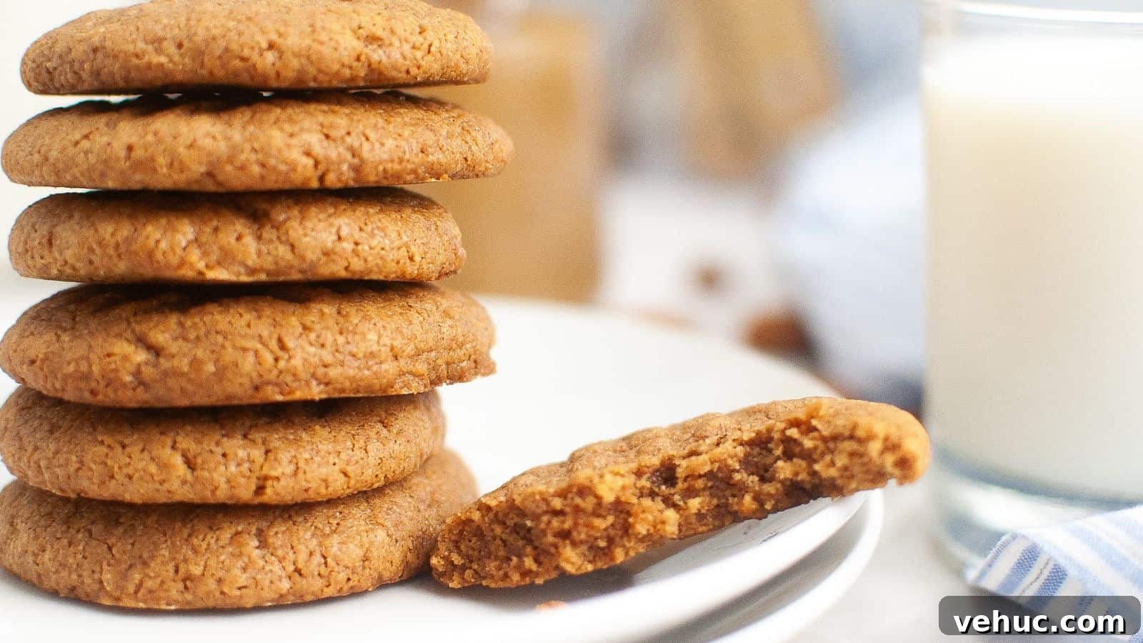 A stack of round cookies on a plate with one cookie partially eaten. A glass of milk is in the background.