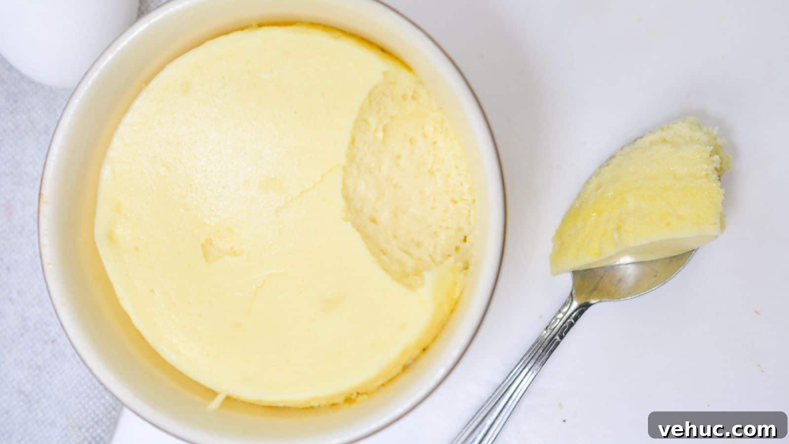 A ramekin of creamy, smooth cheesecake with a spoon resting beside it, taking out a scoop on a white background.