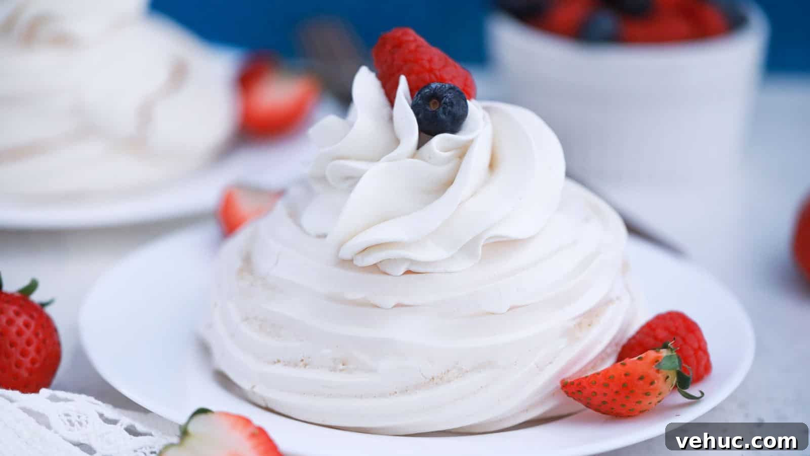 Pavlova dessert with whipped cream and fresh berries on a white plate, garnished with strawberries and blueberries.