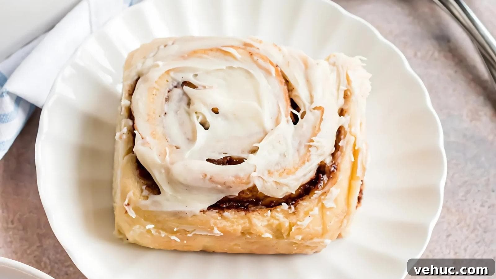 A single cinnamon roll with white icing on top sits on a white plate.