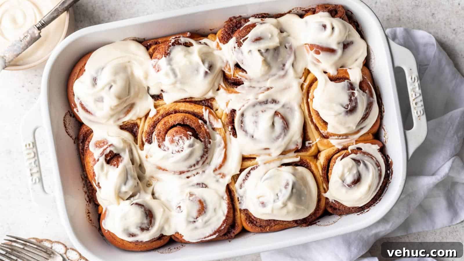 A white baking dish filled with freshly baked cinnamon rolls topped with a thick layer of white icing.