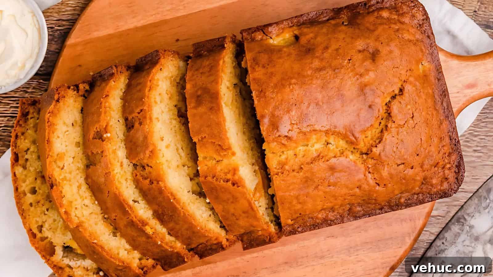 Sliced loaf of banana bread on a wooden board, with a bowl of cream cheese nearby.