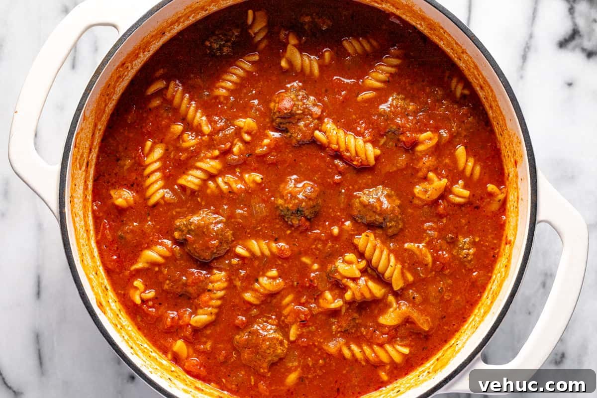 Creamy Italian Meatball Soup: Cozy Weeknight Recipe 7 Large white pot filled with tomato broth, meatballs, and rotini pasta.