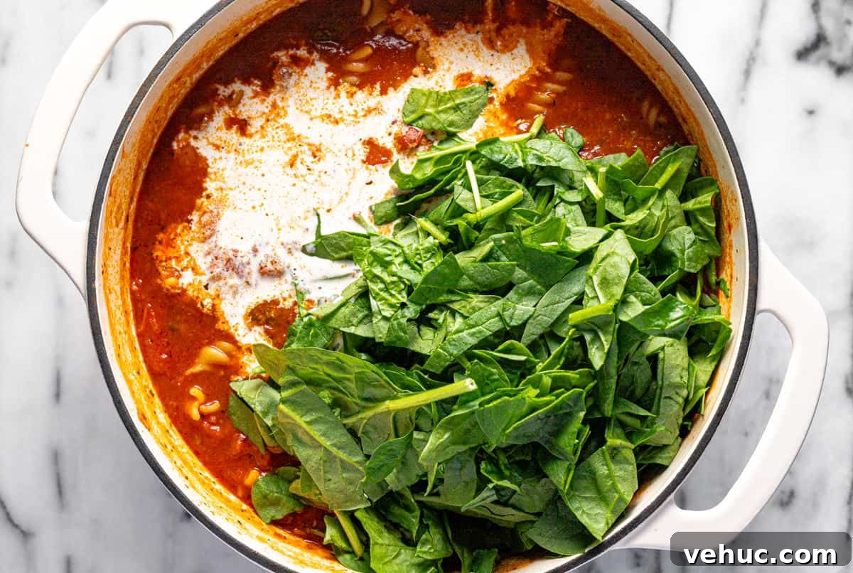 Creamy Italian Meatball Soup: Cozy Weeknight Recipe 8 Spinach and heavy cream being added to a large pot of homemade meatball soup.