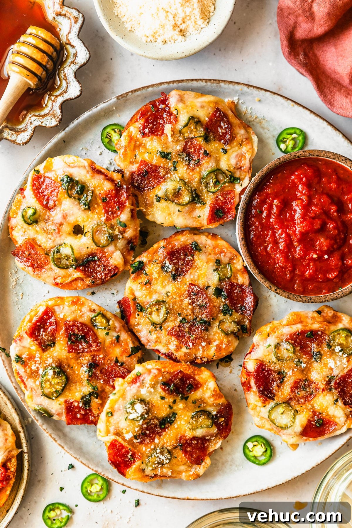 Homemade Pizza Bagel Bites Recipe: Quick Oven & Air Fryer Guide 2 A grey platter of homemade pizza bagel bites on a tan counter next to white bowls of hot honey and parmesan, an orange linen, and glasses of white wine.