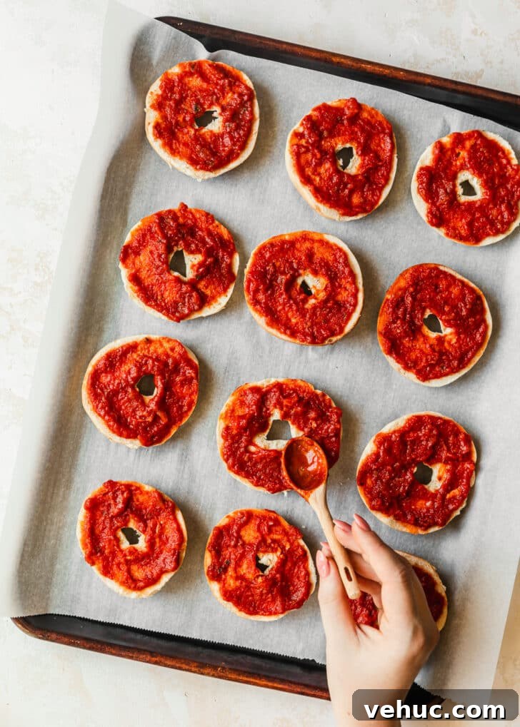 Homemade Pizza Bagel Bites Recipe: Quick Oven & Air Fryer Guide 4 A hand spreading red sauce on bagels.