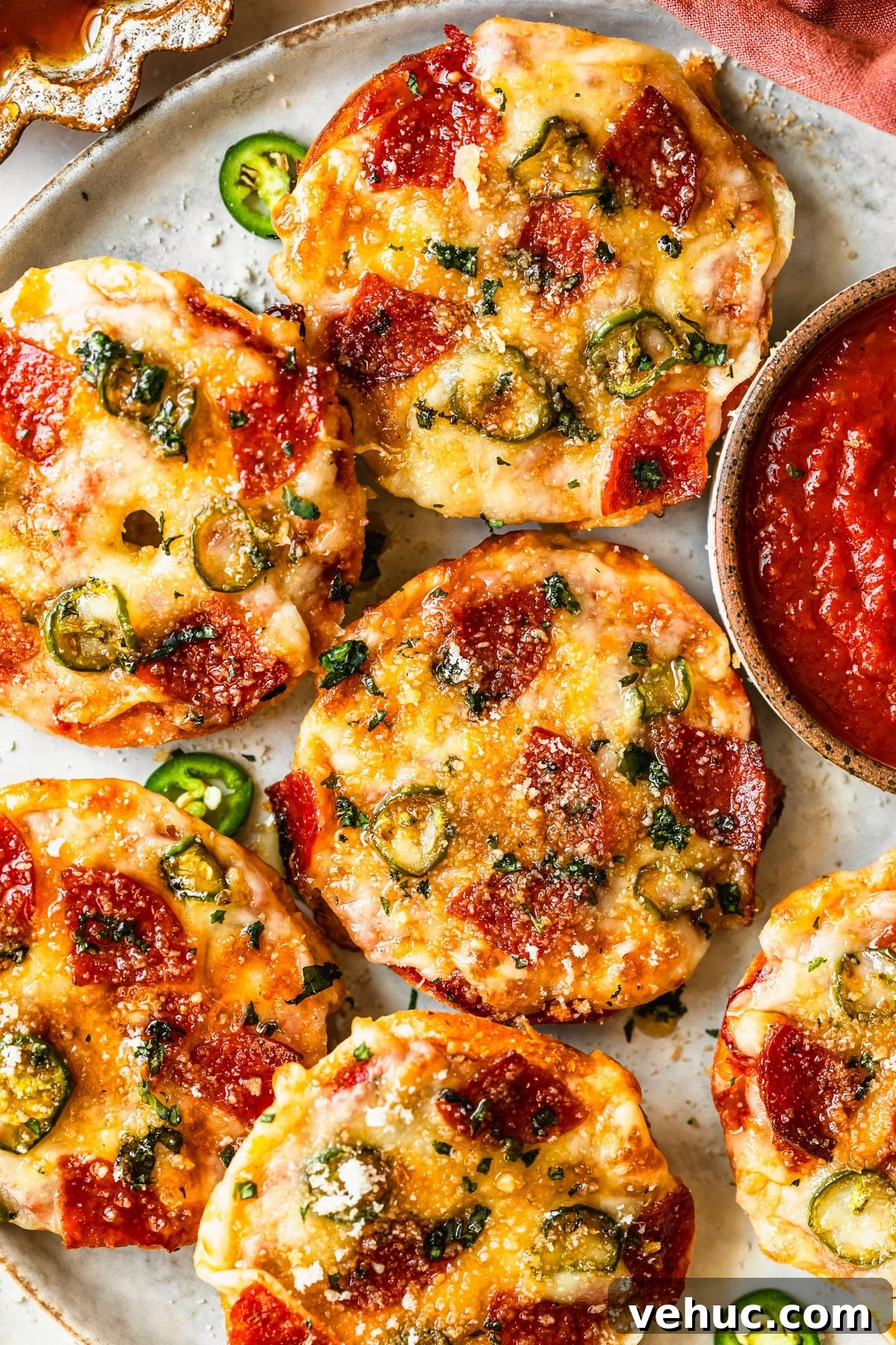 Homemade Pizza Bagel Bites Recipe: Quick Oven & Air Fryer Guide 7 A grey plate of homemade pizza bagel bites on a tan counter next to an orange linen and brown bowl of honey.