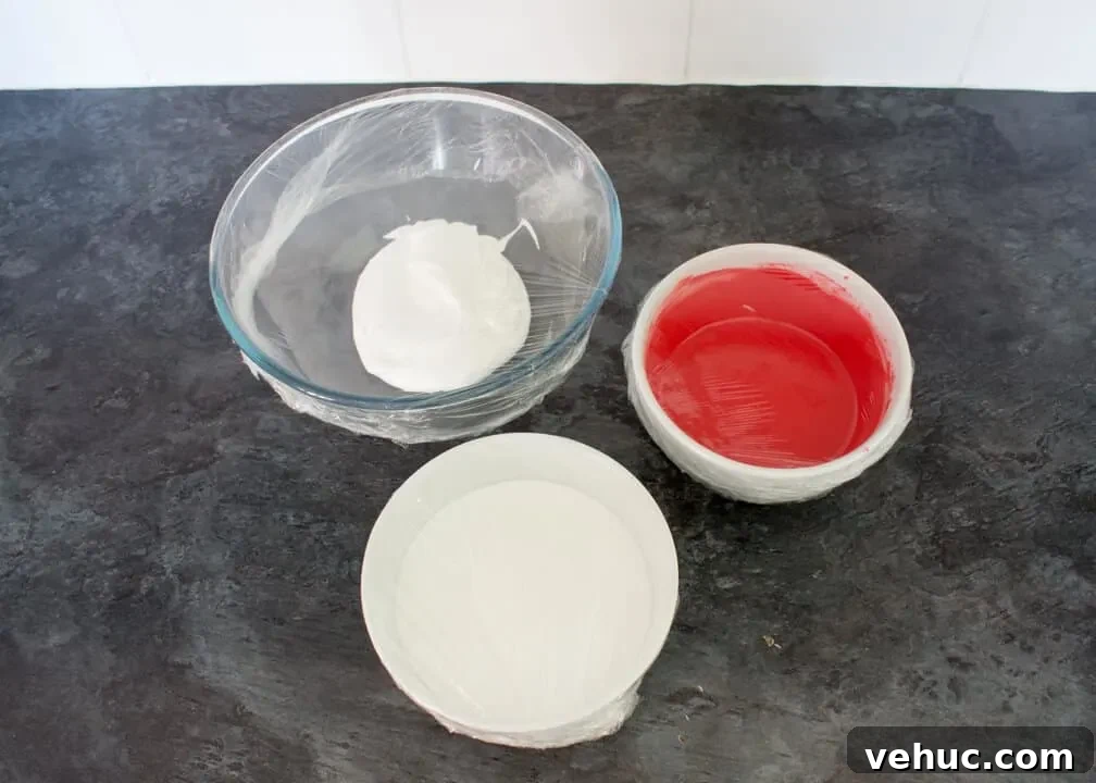 Blood-Spattered Halloween Cookie Ideas for a Spooky Party 7 Red flooding royal icing, white flooding royal icing and white stiffer royal icing in bowls covered with cling film on a kitchen worktop.