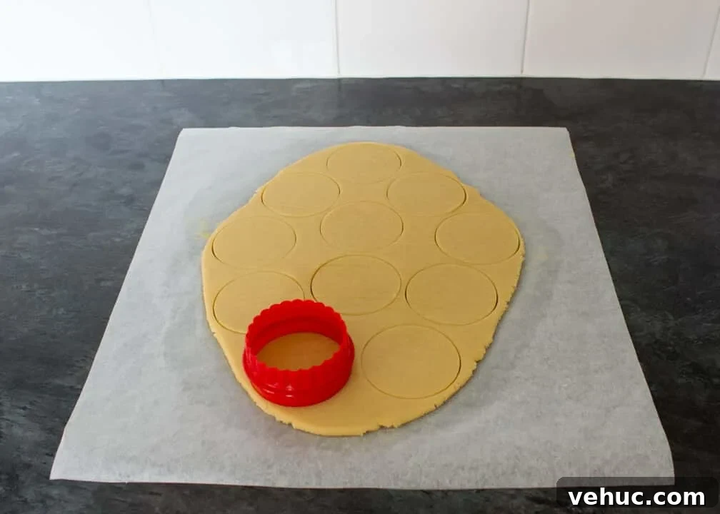 Blood-Spattered Halloween Cookie Ideas for a Spooky Party 8 Cookie dough rolled out on a sheet of baking paper with a cookie cutter having cut out lots of circles.