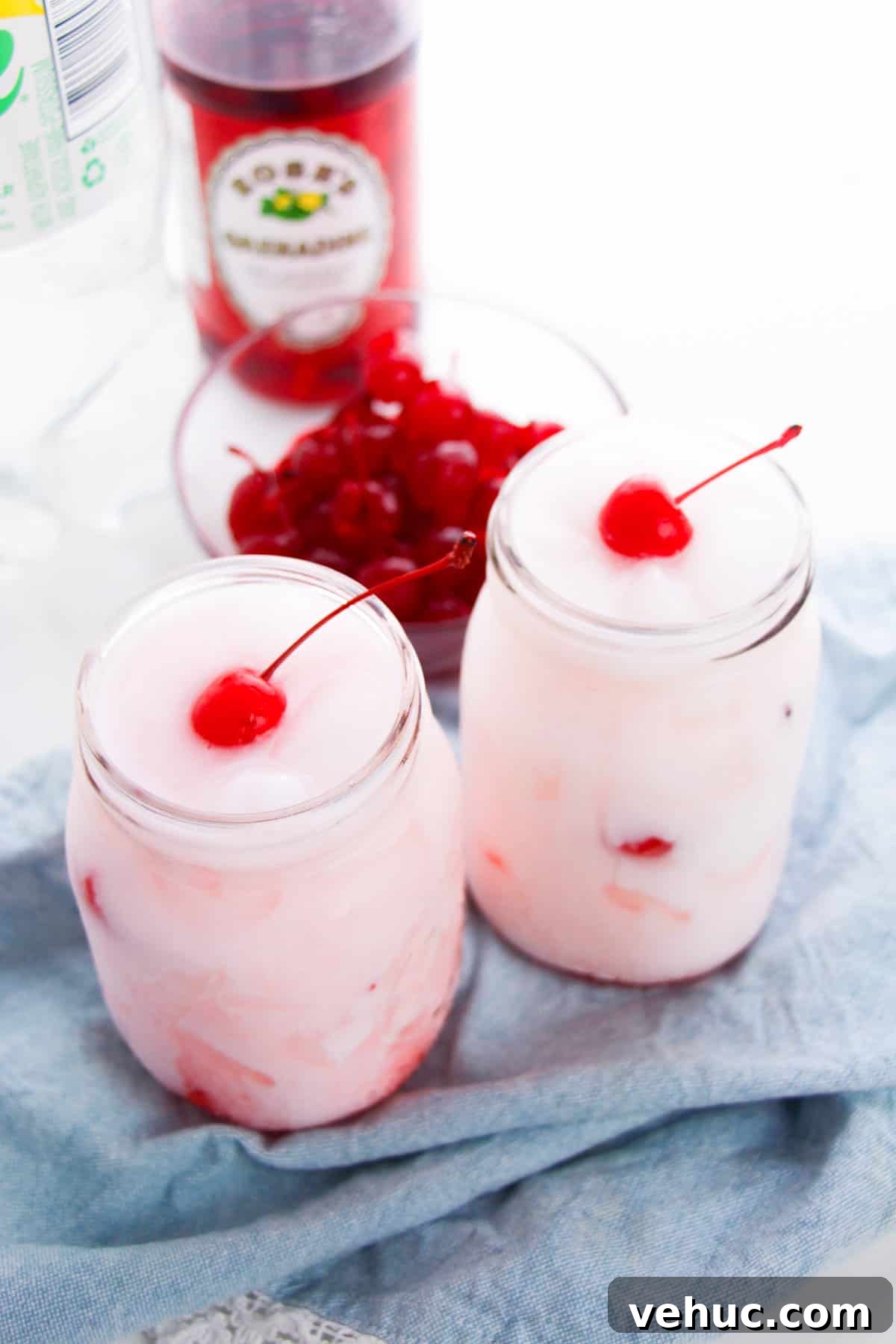 Shirley Temple Dirty Soda Recipe — Sparkling Cherry Lime Mocktail 7 Two Shirley Temple Dirty sodas in mason jars with a bottle of grenadine in the background.