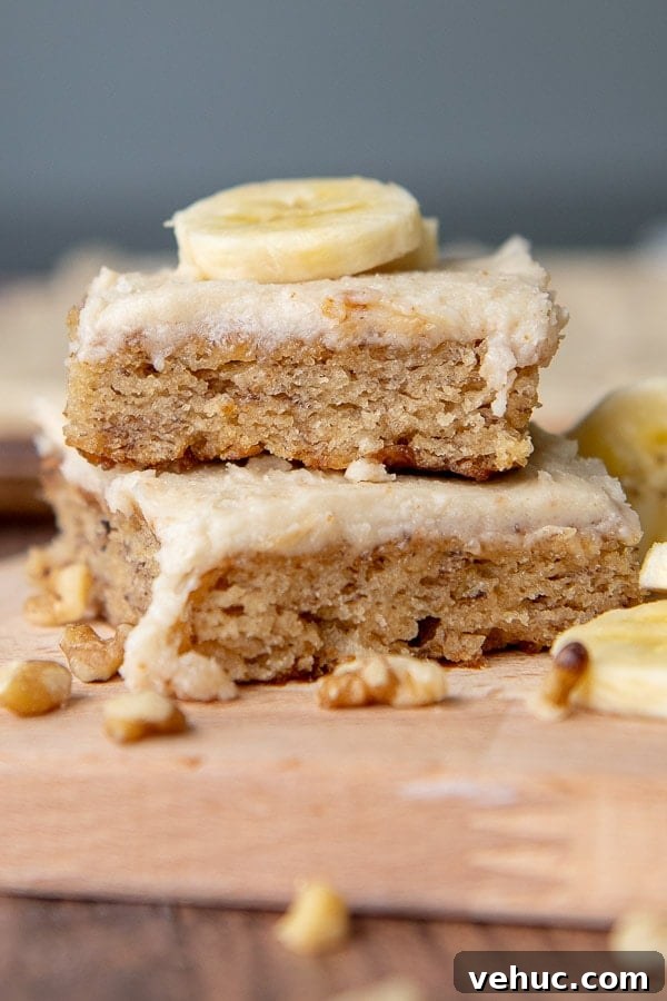 Gluten-Free Banana Bars with Creamy Frosting 2 a stack of two banana bars with a sliced banana piece on top.
