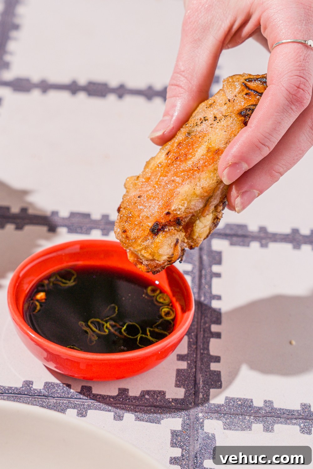 Crispy Rice Paper Veggie Dumplings: Viral TikTok Recipe 12 A hand dipping a veggie rice paper dumpling into a bowl of dipping sauce. The bowl is on a tiled counter.