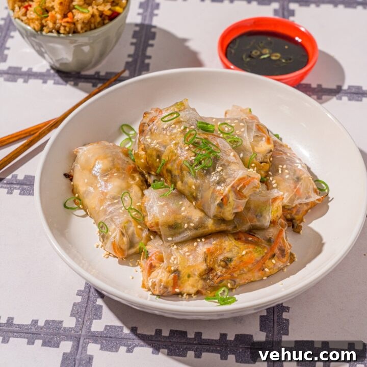 A white bowl with vegetable rice paper dumplings garnished with sliced green onions and sesame seeds. The dumplings are lightly fried. The bowl is on a tiled counter with a pair of chopsticks and small bowl of dipping sauce.