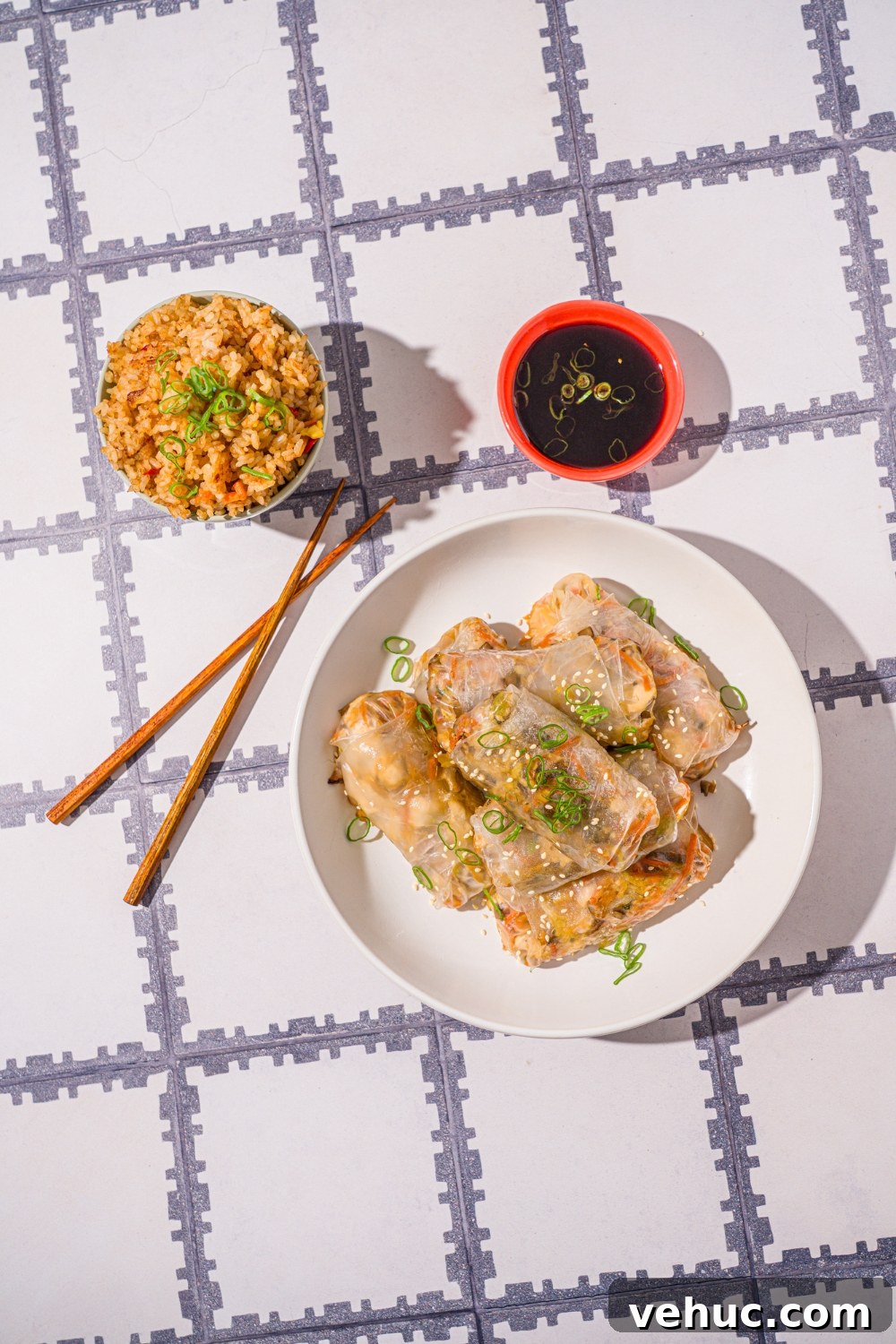 Crispy Rice Paper Veggie Dumplings: Viral TikTok Recipe 10 A white bowl with vegetable rice paper dumplings garnished with sliced green onions and sesame seeds. The dumplings are lightly fried. The bowl is on a tiled counter with a pair of chopsticks and small bowl of dipping sauce.