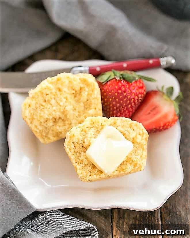 Ina's Corn Muffins - Tender from the buttermilk with a touch of sweetness! Buttermilk Corn Muffin cut in half with a pat of butter on a square white plate.