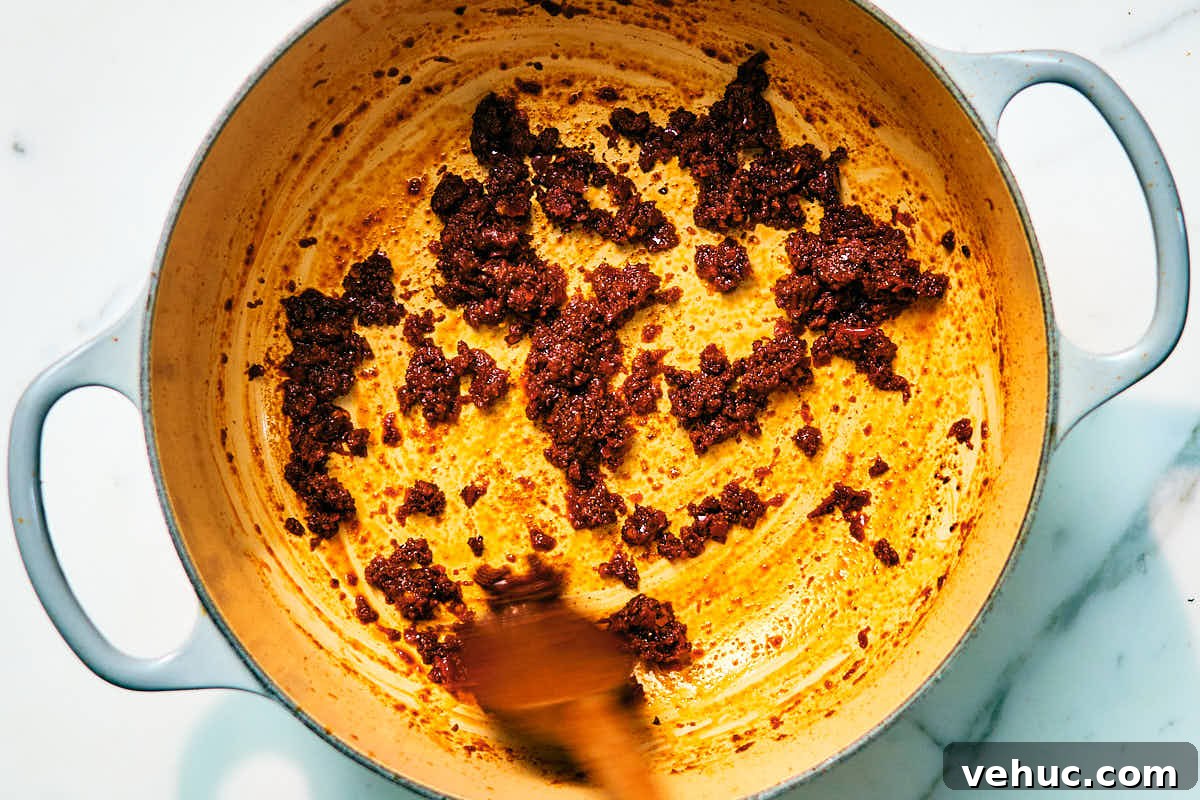Creamy Kabocha Squash and Coconut Milk Soup — No Blender Needed 9 Thai red curry paste and spices being cooked in a pot with a wooden spoon.