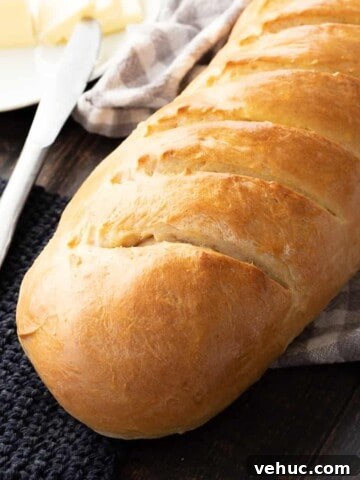 Baked loaf of fluffy french bread on wood table with towel, butter, and knife.