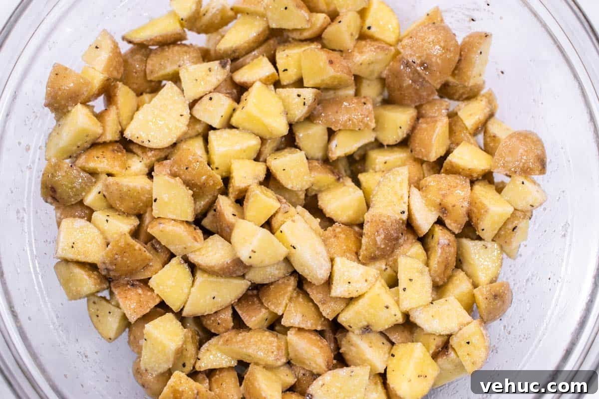 Diced potatoes tossed in seasonings and olive oil in bowl.