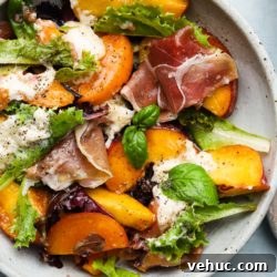 Salad with peaches, burrata, prosciutto, fresh greens, and basil leaves on a plate.