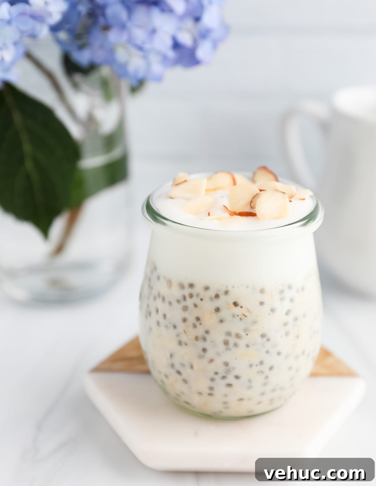Creamy Vanilla Overnight Oats Recipe for Busy Mornings 7 A glass jar on a coaster filled with overnight oats, yogurt, and shaved almonds on top.