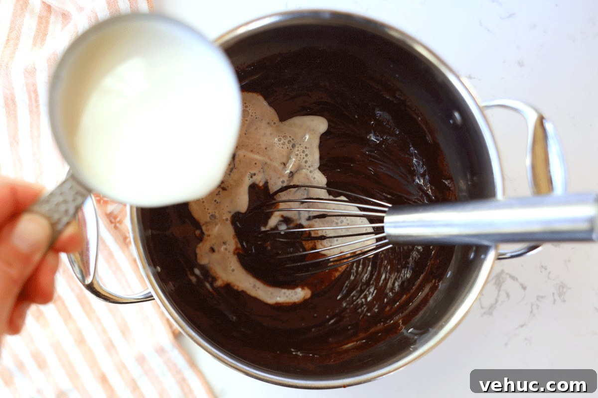 Creamy Homemade Peppermint Hot Chocolate Recipe 3 Milk being poured into melted chocolate. A whisk is in the pot