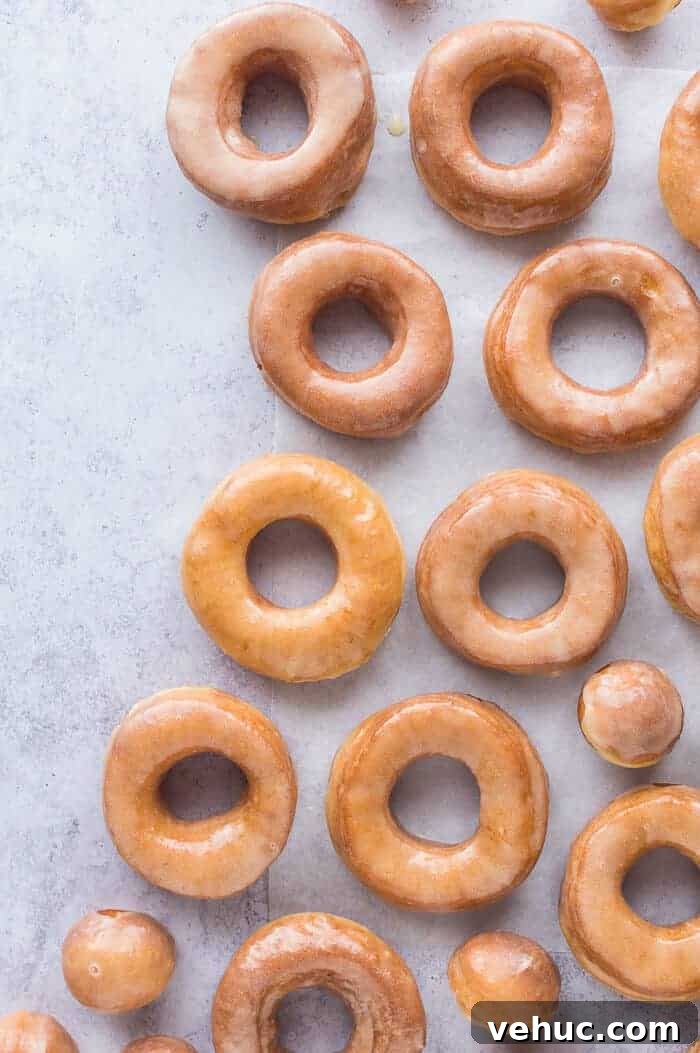 Vegan glazed doughnuts on a sheet of baking parchment on a grey background.