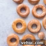 Vegan glazed doughnuts on a sheet of baking parchment on a grey background.
