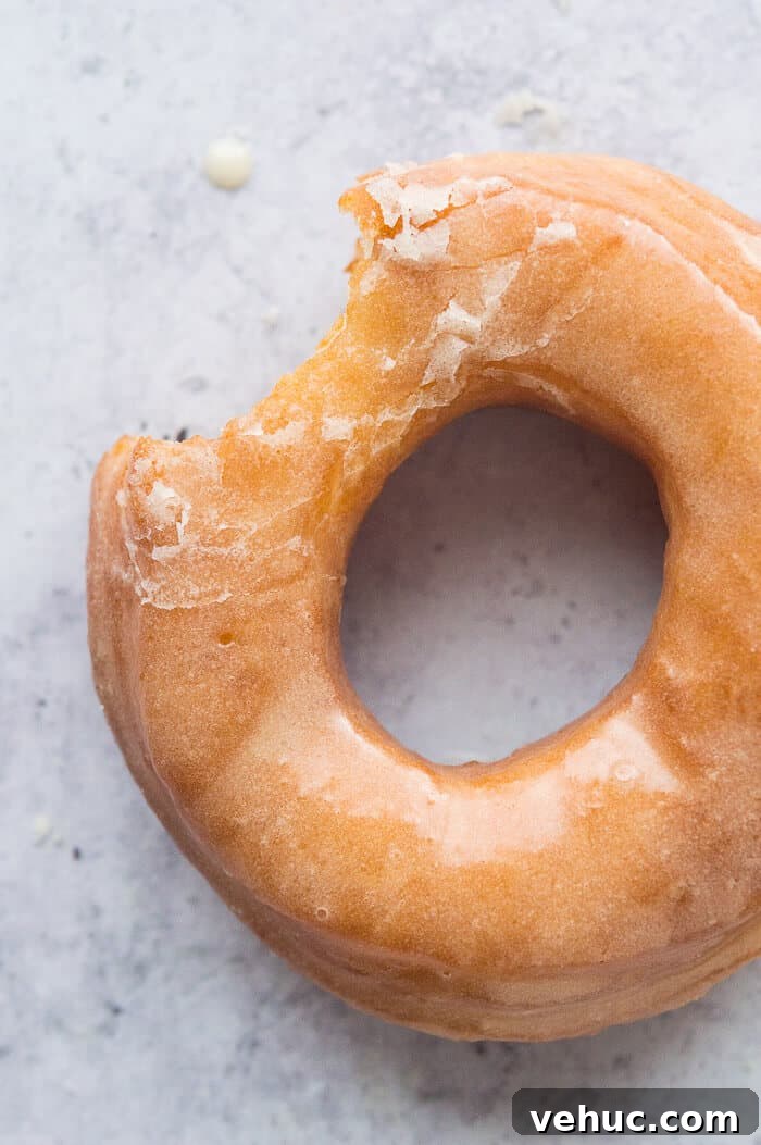 Close up of a glazed vegan fried doughnut with a bite taken out.