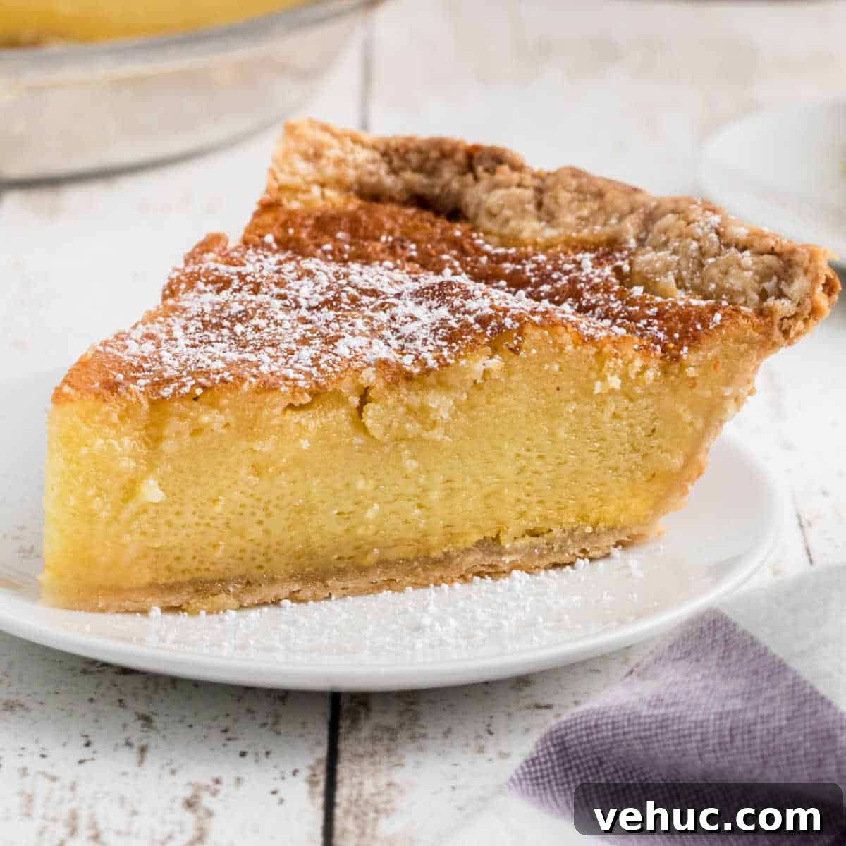 A slice of old fashioned chess pie with a dusting of powdered sugar, cropped square.