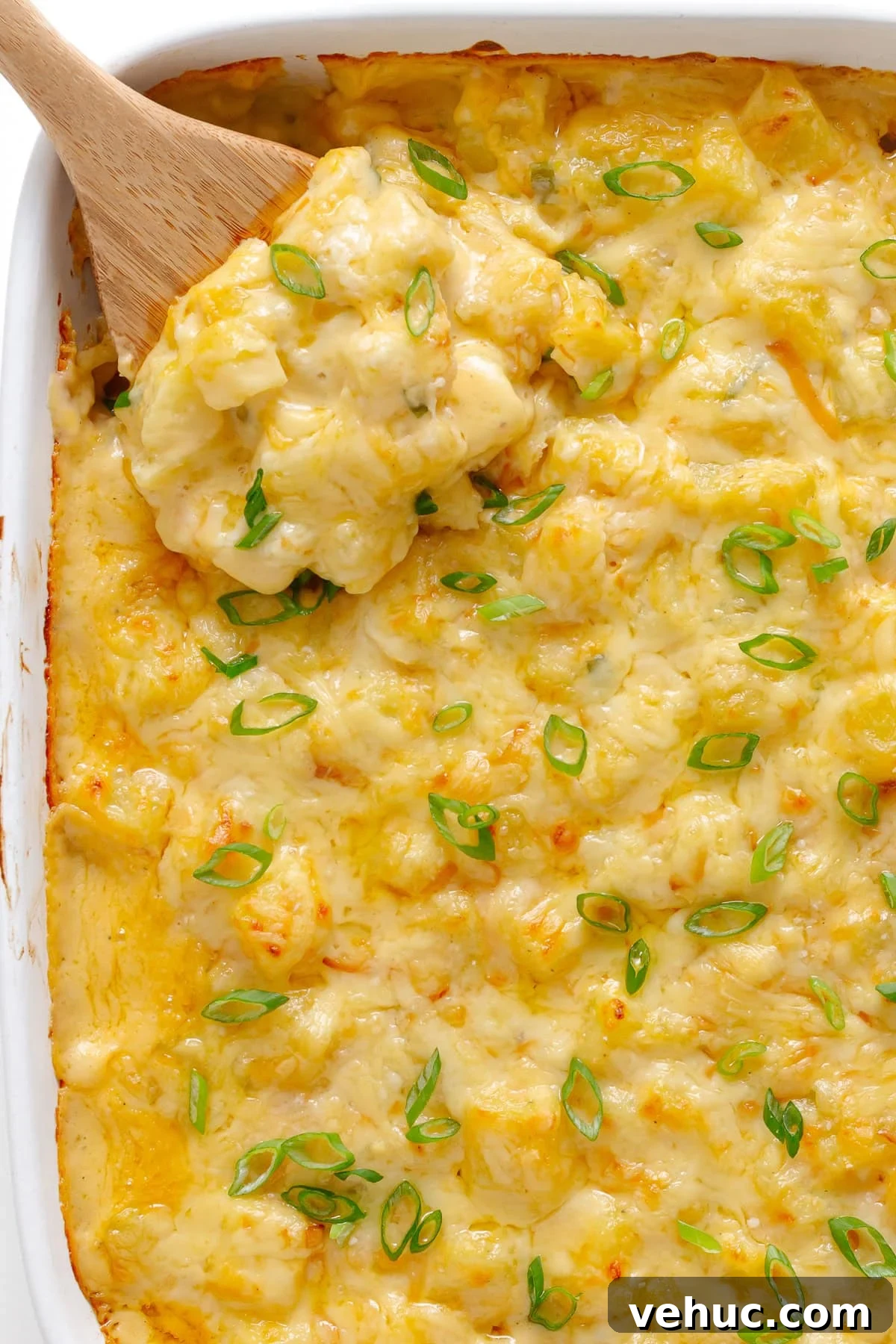 Creamy Cheddar Scalloped Potatoes Recipe 2 Cheesy potatoes in casserole dish with wooden spoon lifting some out.