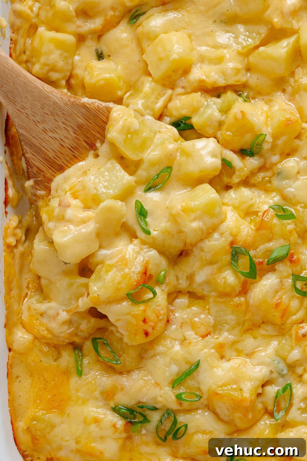 Creamy Cheddar Scalloped Potatoes Recipe 10 Closeup of three cheese potato bake with wooden spoon lifting some out.