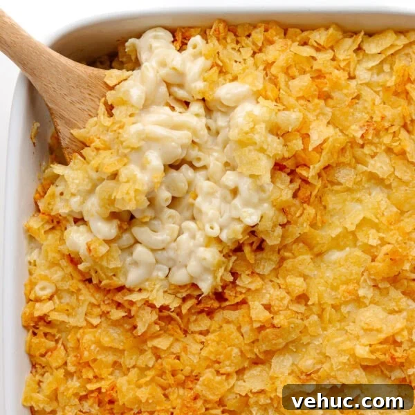 Creamy Cheddar Scalloped Potatoes Recipe 14 Wooden spoon lifting scoop of white cheddar mac and cheese from casserole dish.