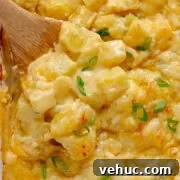 Wooden spoon digging into a baking dish of cheesy potatoes.
