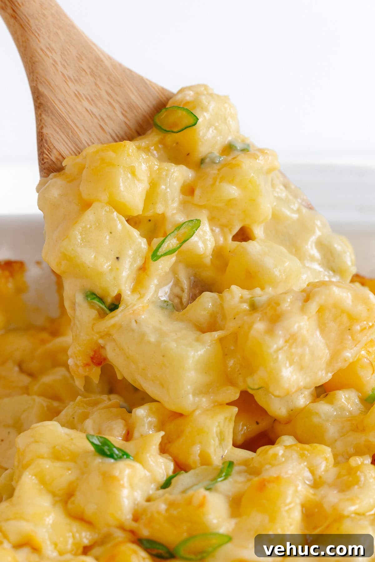 Creamy Cheddar Scalloped Potatoes Recipe 3 Wooden spoon lifting cheesy potatoes from casserole dish.