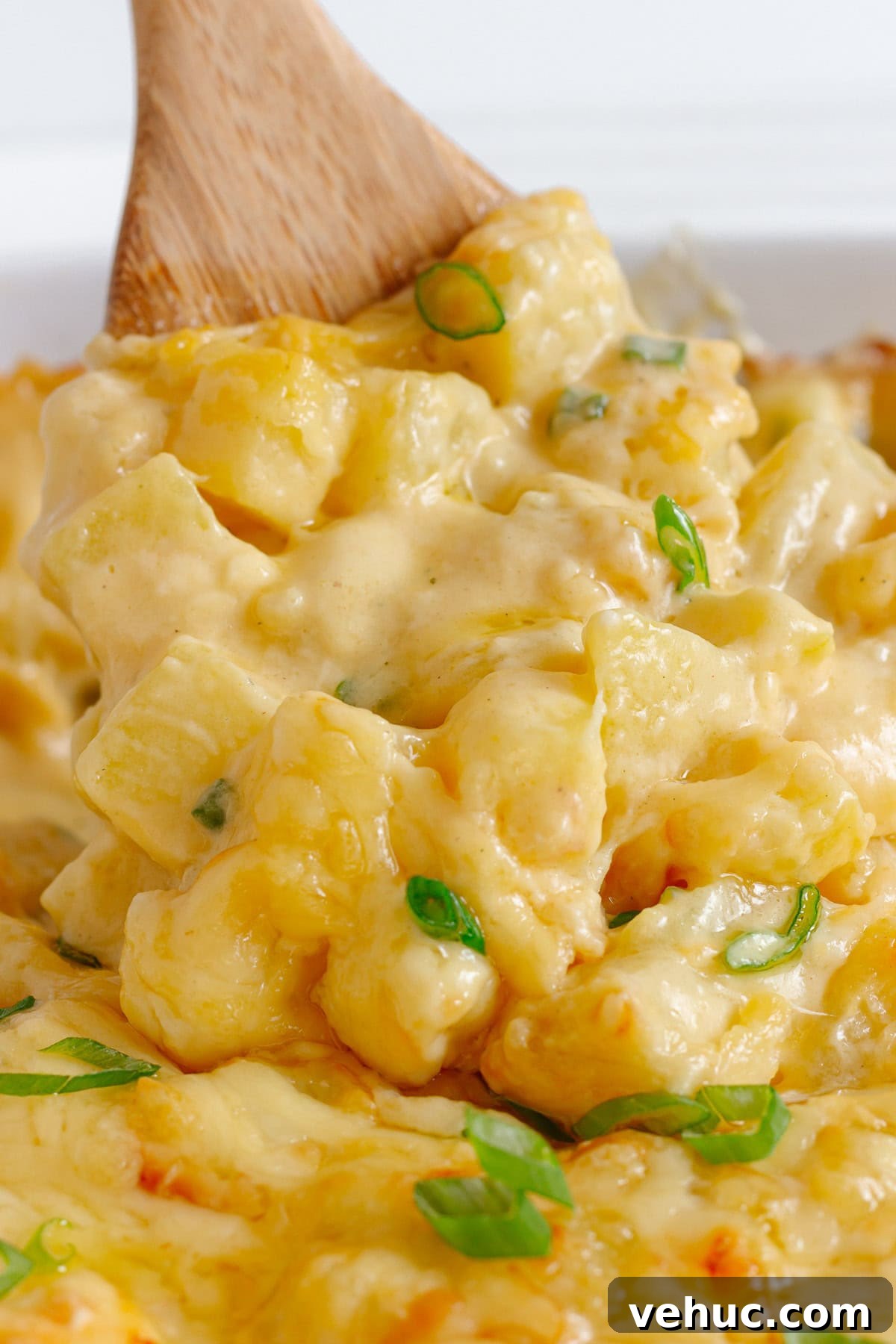 Creamy Cheddar Scalloped Potatoes Recipe 9 Wooden spoon lifting up some cheesy potato bake from casserole dish.